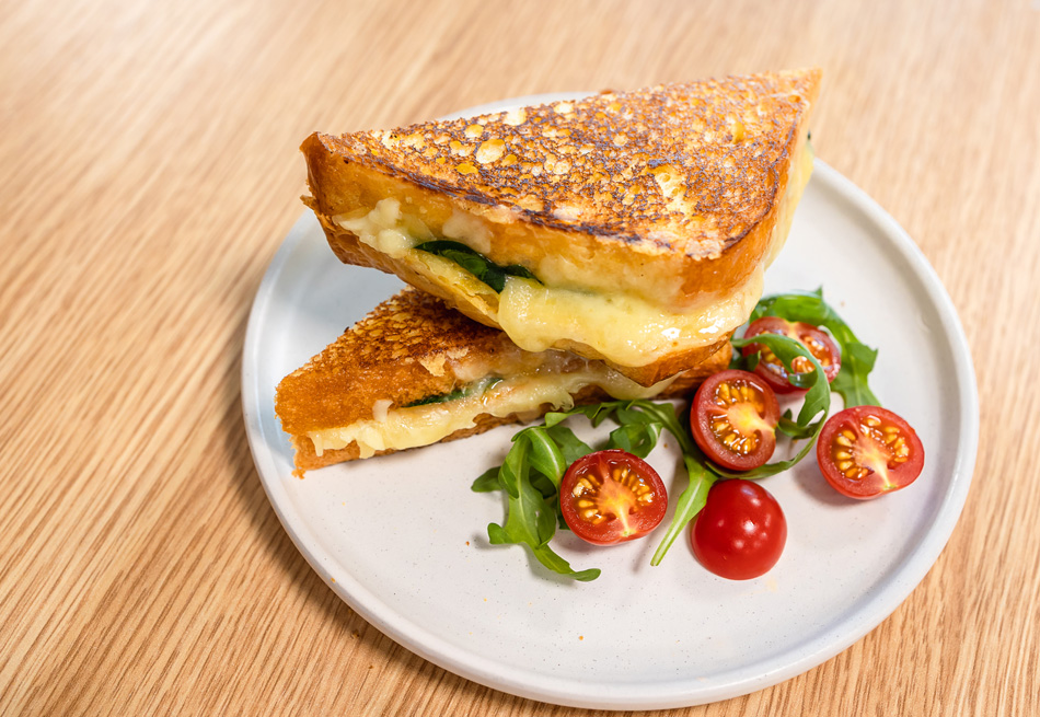 A Brioche Grilled Cheese Sandwich recipe on a white plate next to lettuce and tomatoes